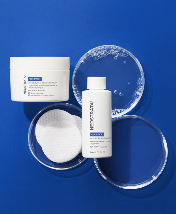 30134_neo_smooth_surface_glycolic_peel_v2_kopia_.jpg Produkten Smooth surface glycolic peel pads representeras mot en blå bakrund, med vätska och bomullspads runt om.