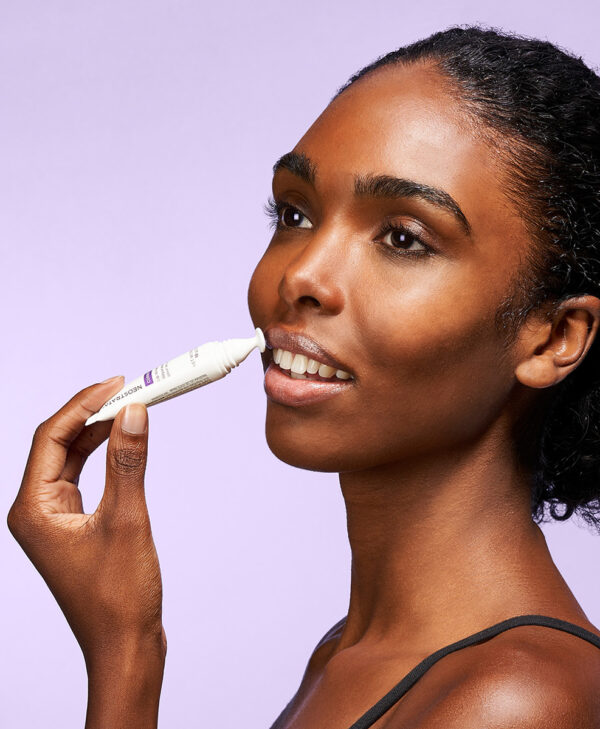 30248_neo_lip_wrinkle_repair_3.jpg Kvinna applicerar läpp produkt mot men lila bakrund.