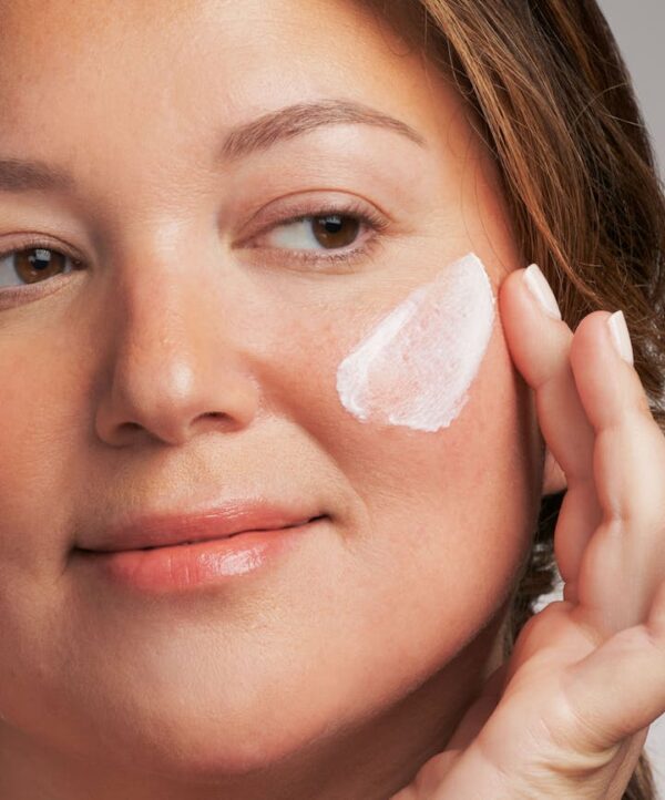 30163_neostrata_sheer_hydration_spf_v4.jpg Vit kräm mot kind på kvinna som håller två fingrar intill sin kind.